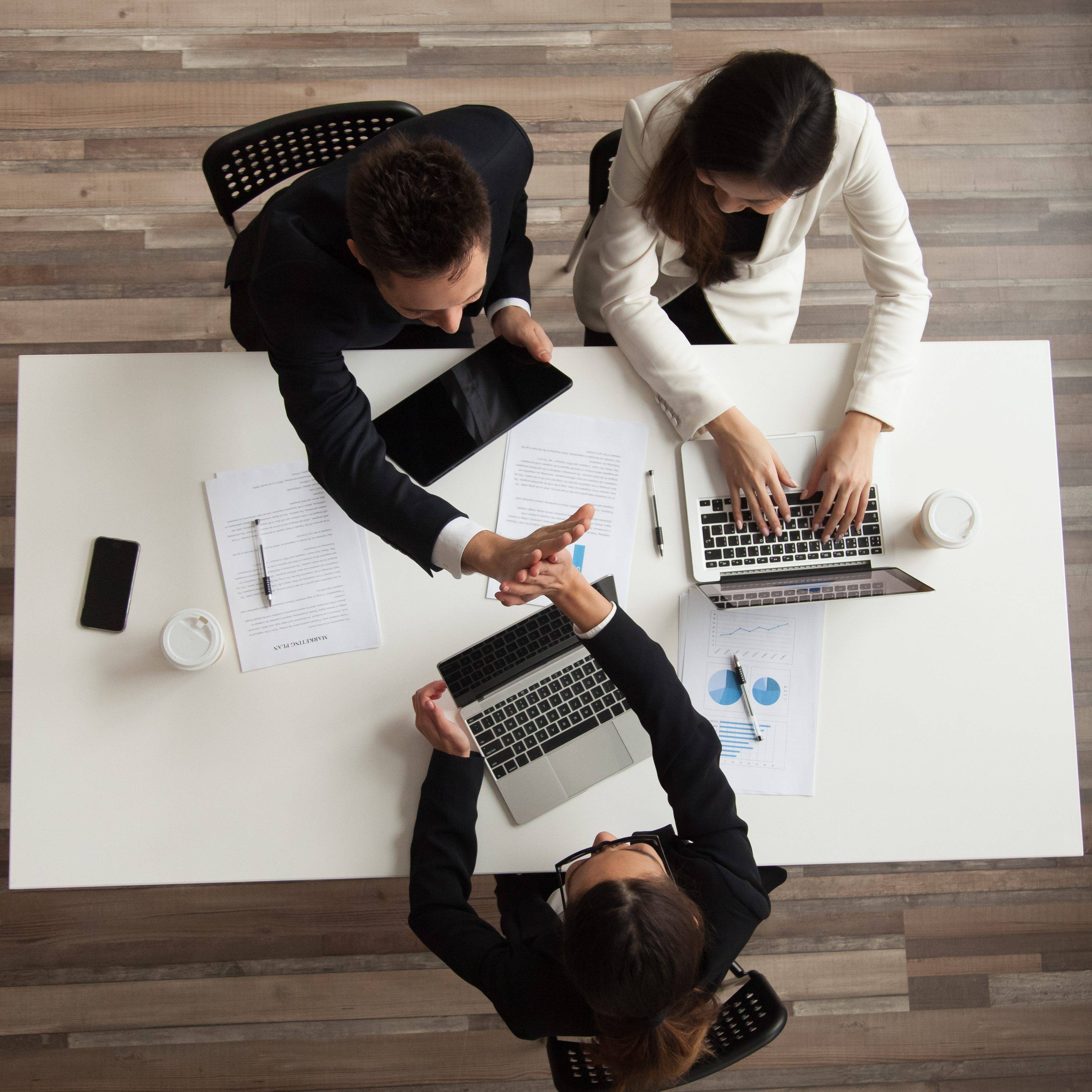 Top view of worker giving high five to colleague Top view of colleagues working together at laptops with handouts, coffee, devices around. Male worker giving high five to female associate during negotiations. Concept of success, teamwork, cooperation